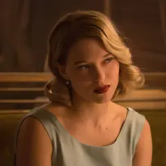 Léa Seydoux w eleganckiej sukience, z burzą blond włosów i czerwoną szminką, przypomina postać z jej filmów.