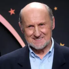 Uśmiechnięty Piotr Fronczewski, znany z wielu niezapomnianych ról w polskich filmach, na tle gwiazd.
