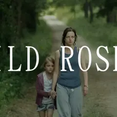 Kobieta i dziewczynka idą ścieżką w lesie. Napis "WILD ROSES" sugeruje, że to kadr z filmu.