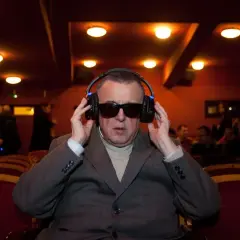 Mężczyzna w okularach i słuchawkach, słucha audiodeskrypcji w kinie.