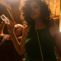 Kobieta w zielonej sukience i mężczyzna pijący z butelki. Scena jak z filmu, pełna zabawy i emocji.