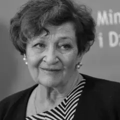 Uśmiechnięta Ewa Dałkowska, aktorka znana z wielu filmów, w eleganckiej stylizacji.