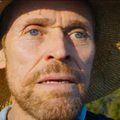 Willem Dafoe jako Van Gogh u Bram Wieczności, z niebieskimi oczami i słomkowym kapeluszem, wpatruje się w dal.