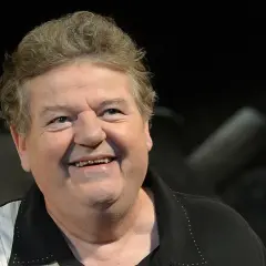 Uśmiechnięty Robbie Coltrane, który grał Hagrida, w czarnej koszuli z białymi pasami.