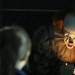 Przerażający klaun Pennywise z "To" w jednym z najlepszych horrorów ostatnich lat, świeci sobie zapalniczką.