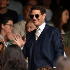 Tom Cruise w garniturze, w okularach przeciwsłonecznych, macha do publiczności. Zastanawiasz się, ile zarabia Tom Cruise?