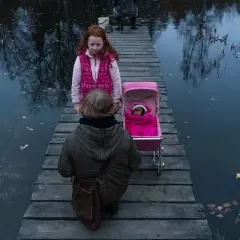 Dwie dziewczynki na drewnianym pomoście, jedna z wózkiem dla lalek, druga obok. Scena jak z filmu "ciemno prawie noc".