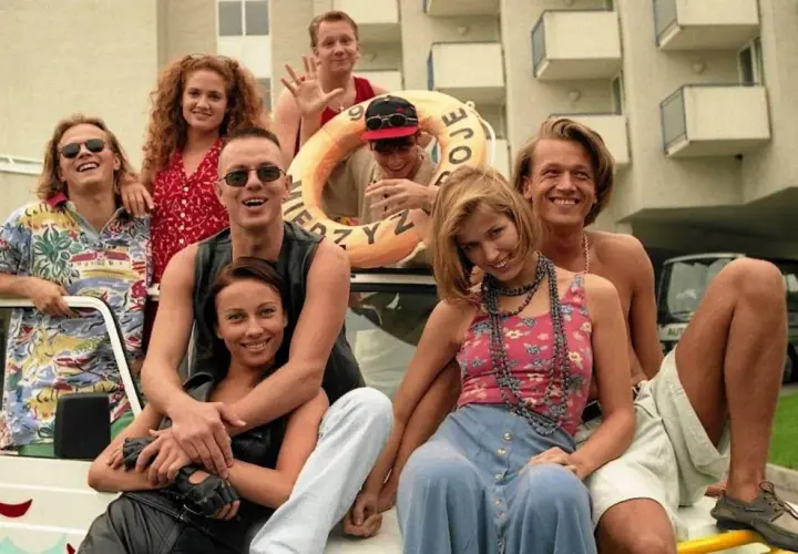 Uśmiechnięci ludzie na tle hotelu, jak z kultowych polskich filmów z lat 90. Wesoła ekipa gotowa na przygodę.