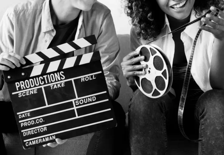 Dwie osoby trzymają klaps filmowy i rolkę taśmy filmowej. Zastanawiasz się, ile zarabia producent filmowy?
