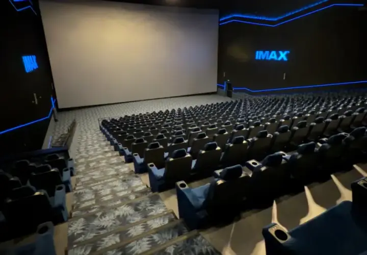 Pusta sala kinowa IMAX z ogromnym ekranem i rzędami niebieskich foteli. To właśnie co to znaczy IMAX w kinie – niesamowite wrażenia wizualne.