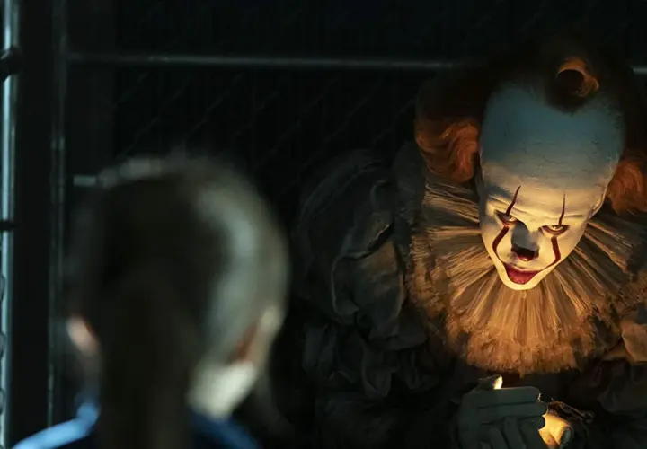 Przerażający klaun Pennywise z "To" w jednym z najlepszych horrorów ostatnich lat, świeci sobie zapalniczką.