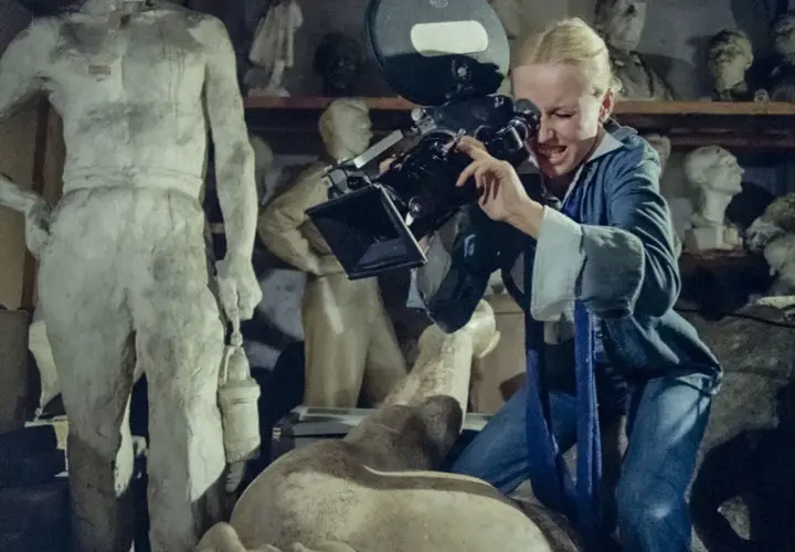Kobieta z kamerą w pracowni rzeźbiarskiej, jak z filmów Feliksa Falka. W tle antyczne posągi.