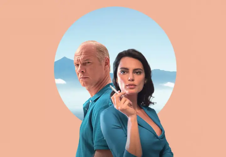 Para z filmu "La Gomera" na tle gór i nieba. Mężczyzna z siwymi włosami i kobieta z papierosem w dłoni.