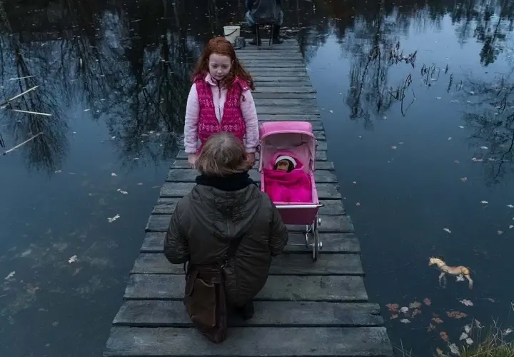 Dwie dziewczynki na drewnianym pomoście, jedna z wózkiem dla lalek, druga obok. Scena jak z filmu "ciemno prawie noc".