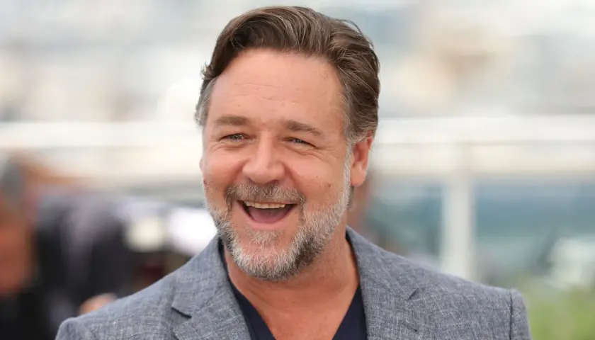 Uśmiechnięty Russell Crowe w szarym garniturze. Zastanawiasz się, ile lat ma Russell Crowe?