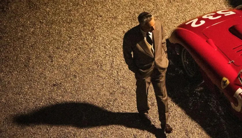 Mężczyzna w garniturze stoi obok czerwonego Ferrari. Zapowiedź filmu "Ferrari" budzi emocje, jak te wyścigi.