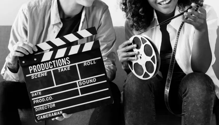 Dwie osoby trzymają klaps filmowy i rolkę taśmy filmowej. Zastanawiasz się, ile zarabia producent filmowy?