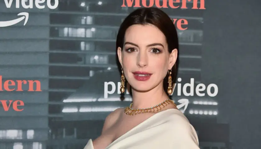 Anne Hathaway, której wiek jest często przedmiotem dyskusji, prezentuje się olśniewająco w złotej biżuterii na tle logo Amazon Prime Video.