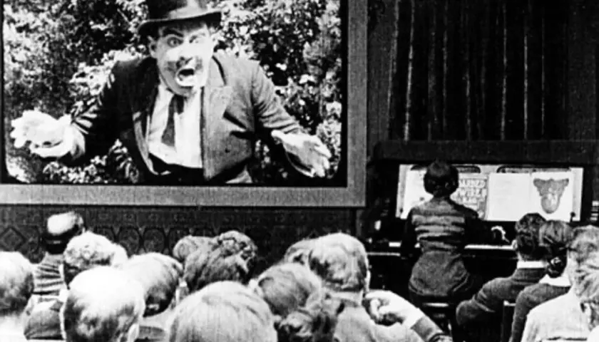 Widownia w kinie ogląda pierwszy film z dźwiękiem. Na ekranie aktor w cylindrze krzyczy, a obok gra muzyk.