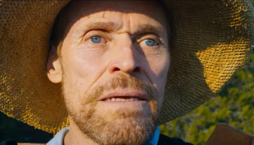 Willem Dafoe jako Van Gogh u Bram Wieczności, z niebieskimi oczami i słomkowym kapeluszem, wpatruje się w dal.