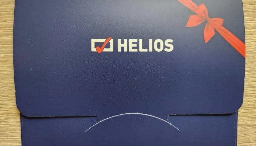 Chcesz wiedzieć, ile kosztuje voucher do kina Helios? Na zdjęciu widać elegancką, granatową kopertę z logo Helios i czerwoną wstążką, idealną na prezent.