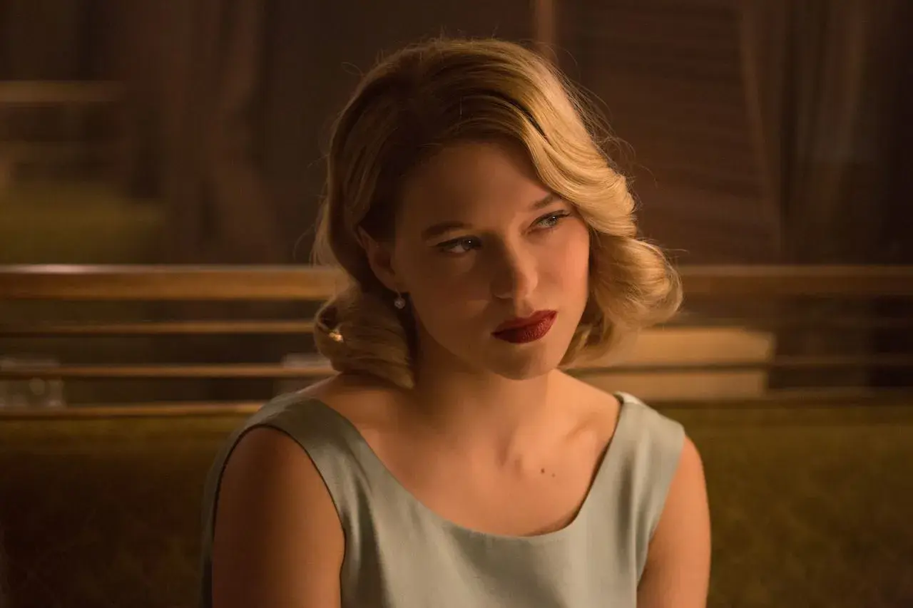 Léa Seydoux w eleganckiej sukience, z burzą blond włosów i czerwoną szminką, przypomina postać z jej filmów.