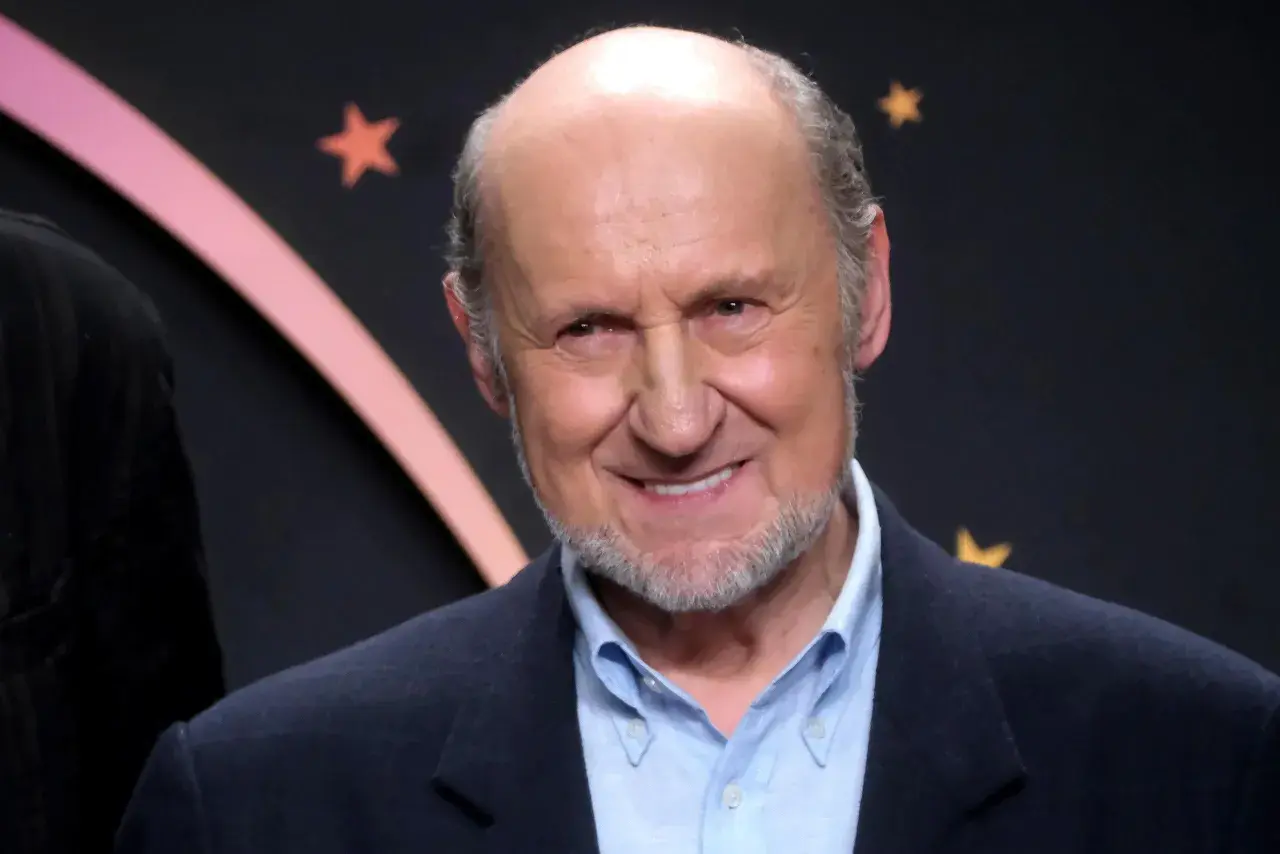 Uśmiechnięty Piotr Fronczewski, znany z wielu niezapomnianych ról w polskich filmach, na tle gwiazd.