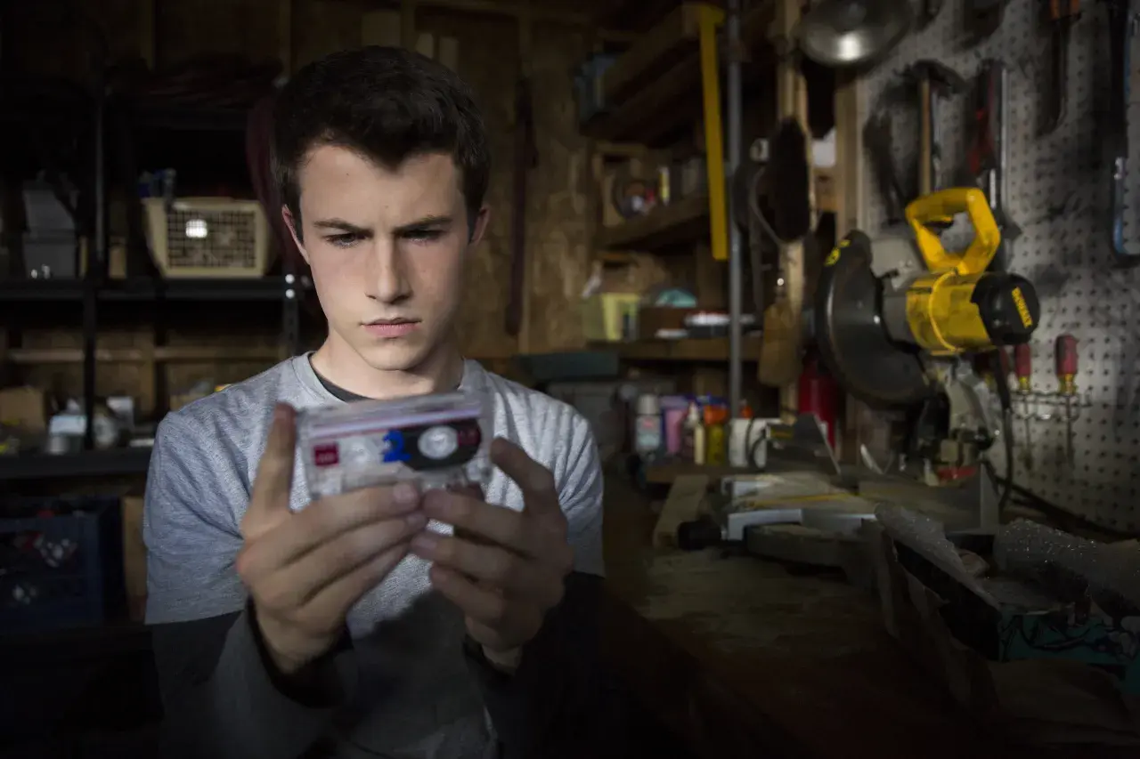 Clay Jensen z serialu "13 powodów" trzyma kasetę z nagraniem w warsztacie pełnym narzędzi.