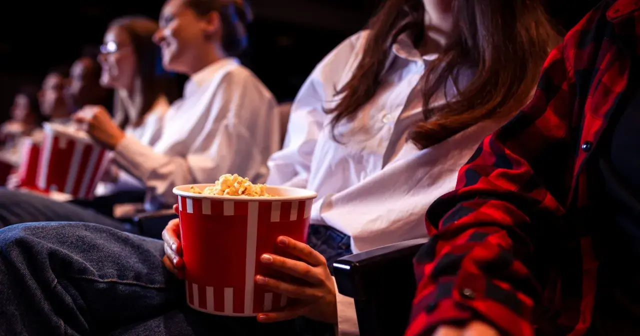 Ludzie w kinie jedzą popcorn. Zastanawiasz się, ile kosztują nachosy w kinie?