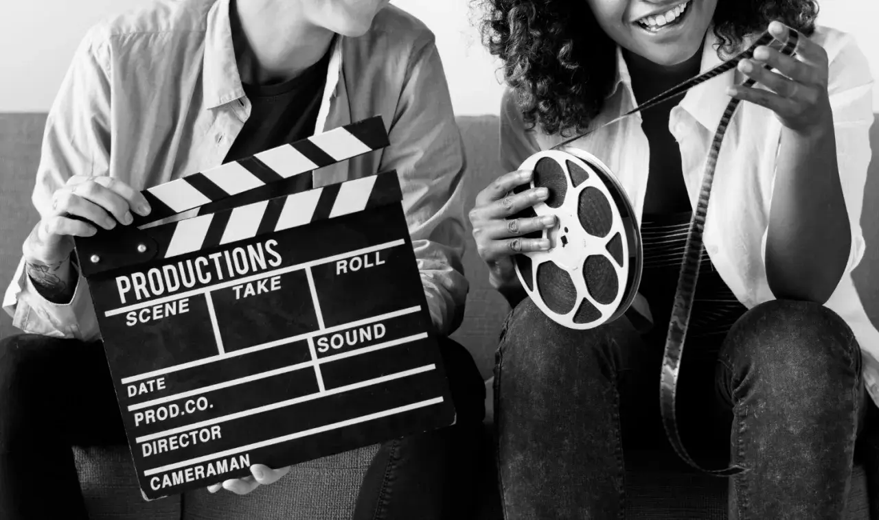 Dwie osoby trzymają klaps filmowy i rolkę taśmy filmowej. Zastanawiasz się, ile zarabia producent filmowy?