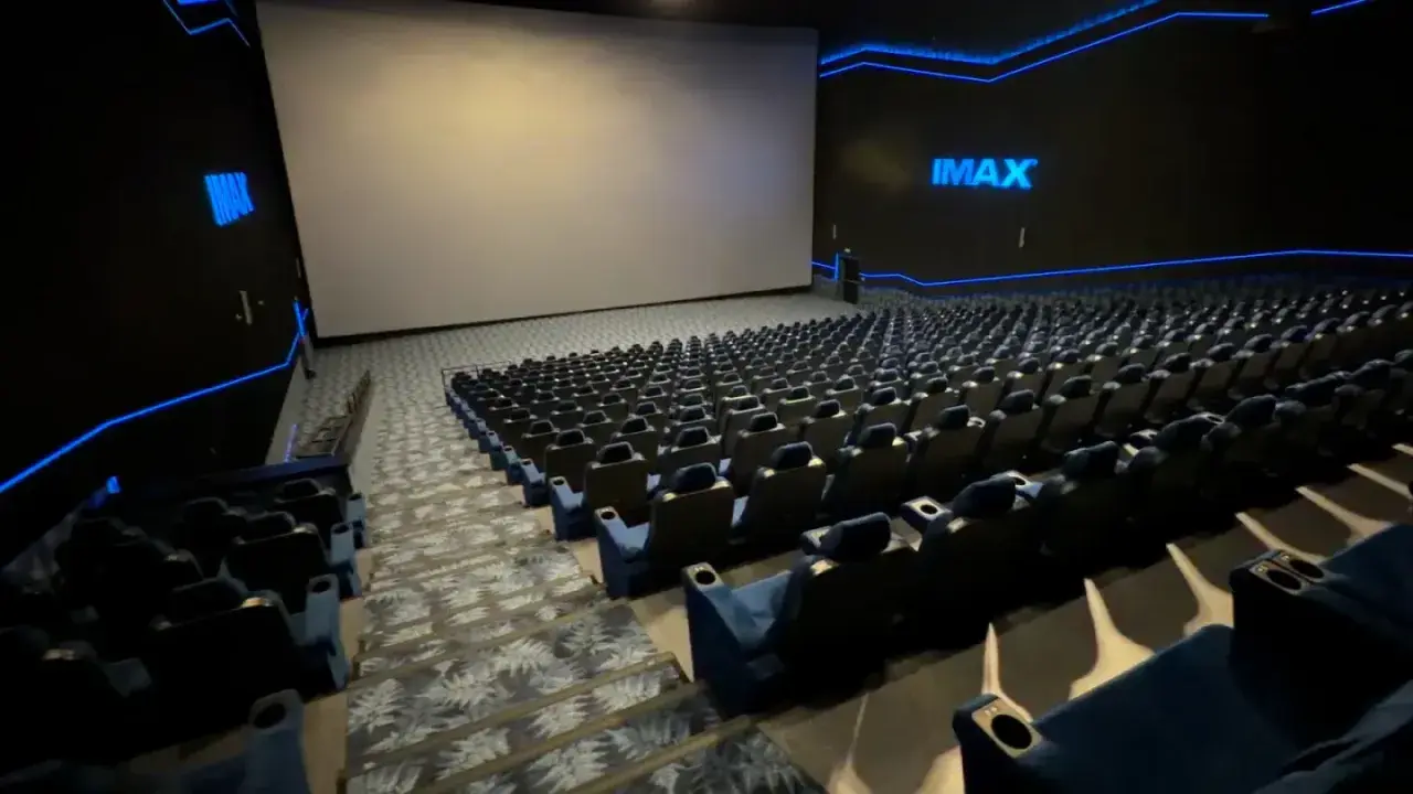Pusta sala kinowa IMAX z ogromnym ekranem i rzędami niebieskich foteli. To właśnie co to znaczy IMAX w kinie – niesamowite wrażenia wizualne.