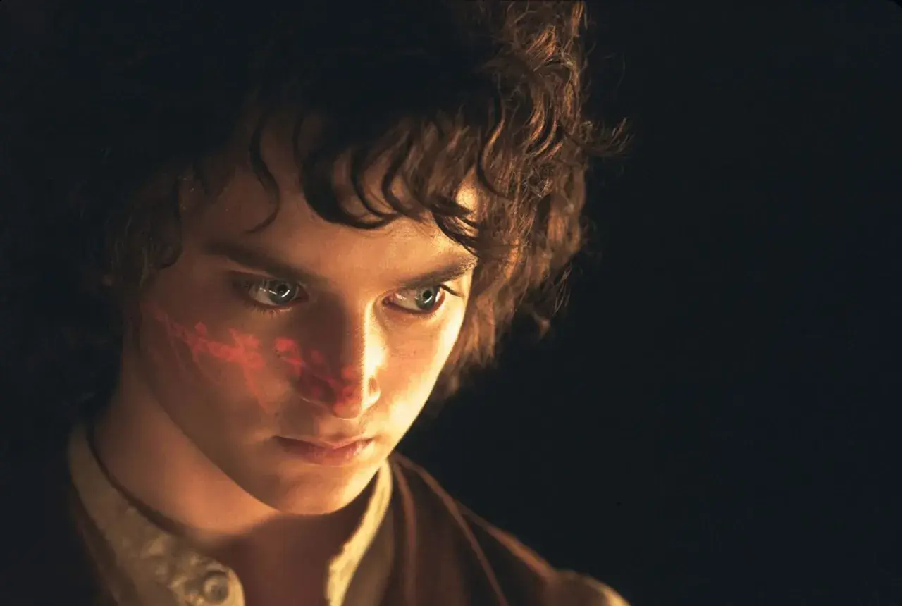 Elijah Wood, kto gra Frodo Bagginsa, z czerwonym znakiem na policzku, w ciemności.