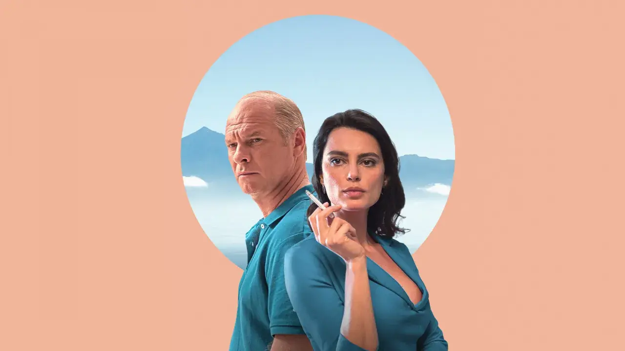 Para z filmu "La Gomera" na tle gór i nieba. Mężczyzna z siwymi włosami i kobieta z papierosem w dłoni.
