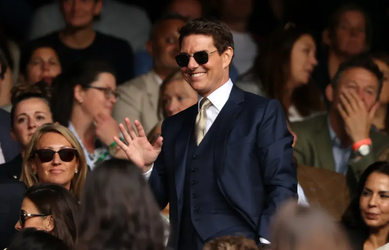 Tom Cruise w garniturze, w okularach przeciwsłonecznych, macha do publiczności. Zastanawiasz się, ile zarabia Tom Cruise?