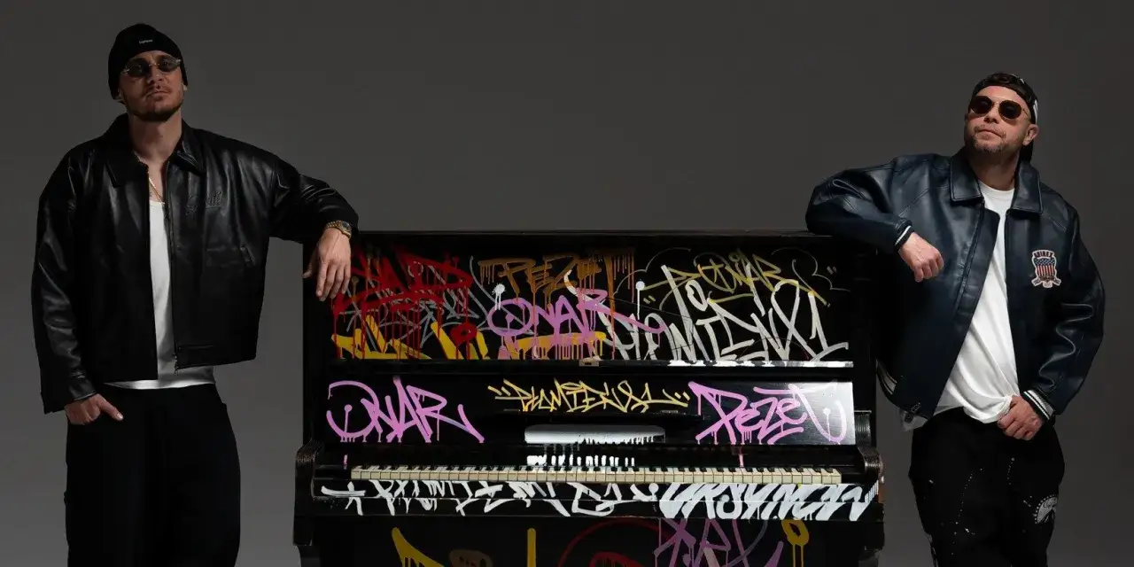 Dwóch mężczyzn w skórzanych kurtkach opiera się o pianino pokryte graffiti. Dźwięki muzyki unoszą się jakby 300 metrów nad ziemią.