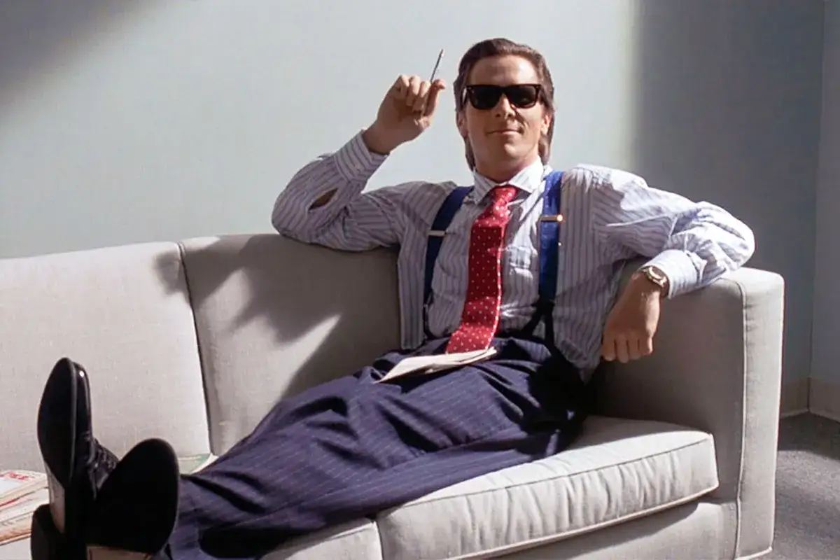 Patrick Bateman w okularach przeciwsłonecznych, na kanapie, z papierosem w dłoni. Czy Patrick Bateman naprawde zabijał? To pytanie pozostaje bez odpowiedzi.