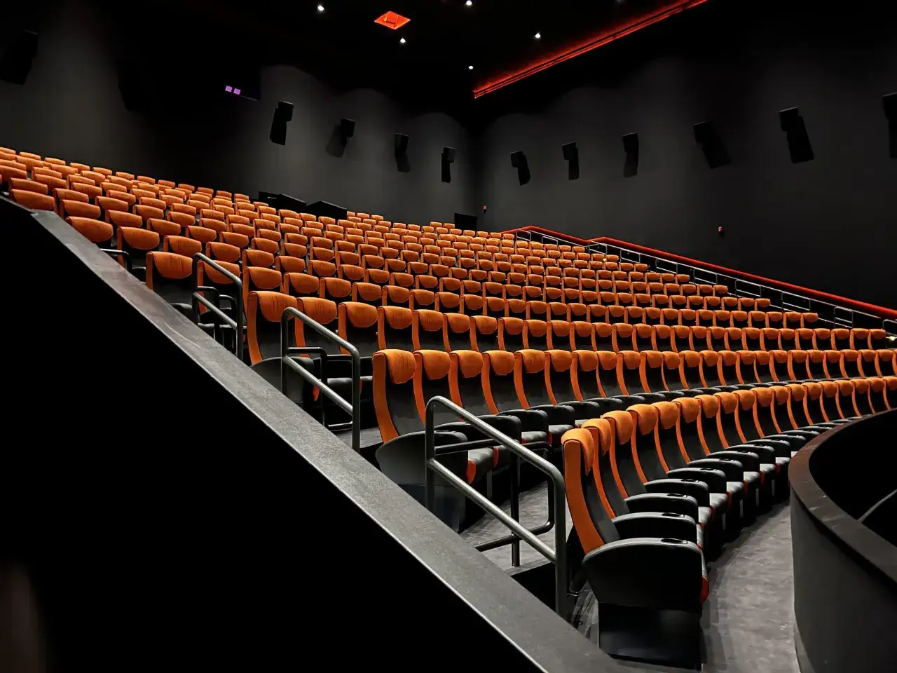 Puste, pomarańczowo-czarne fotele kinowe w sali. Wyobraź sobie, co to jest 4DX – to właśnie tu poczujesz film całym sobą!