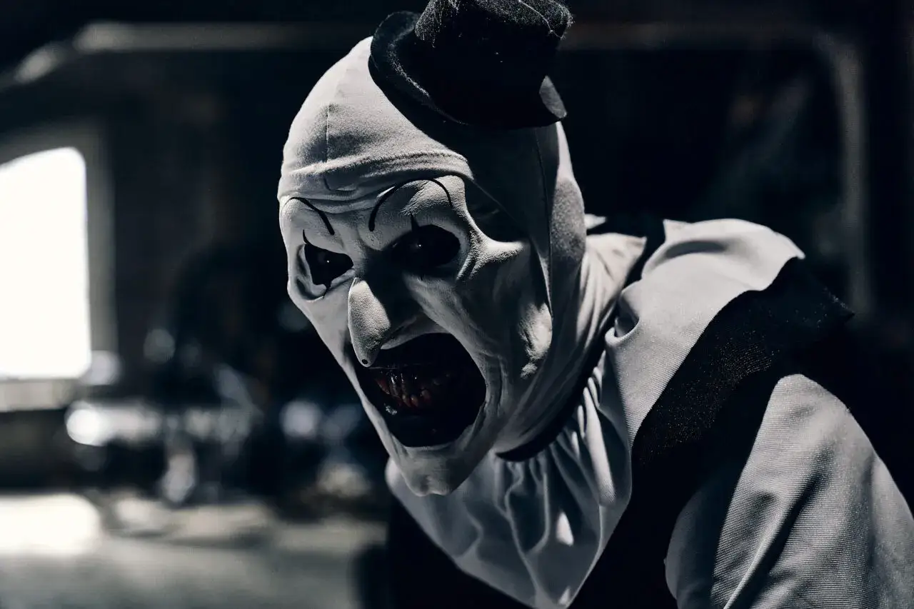 Przerażający Art the Clown w kinie. Zbliżenie na makabryczną maskę i otwarte usta z krwawymi zębami.