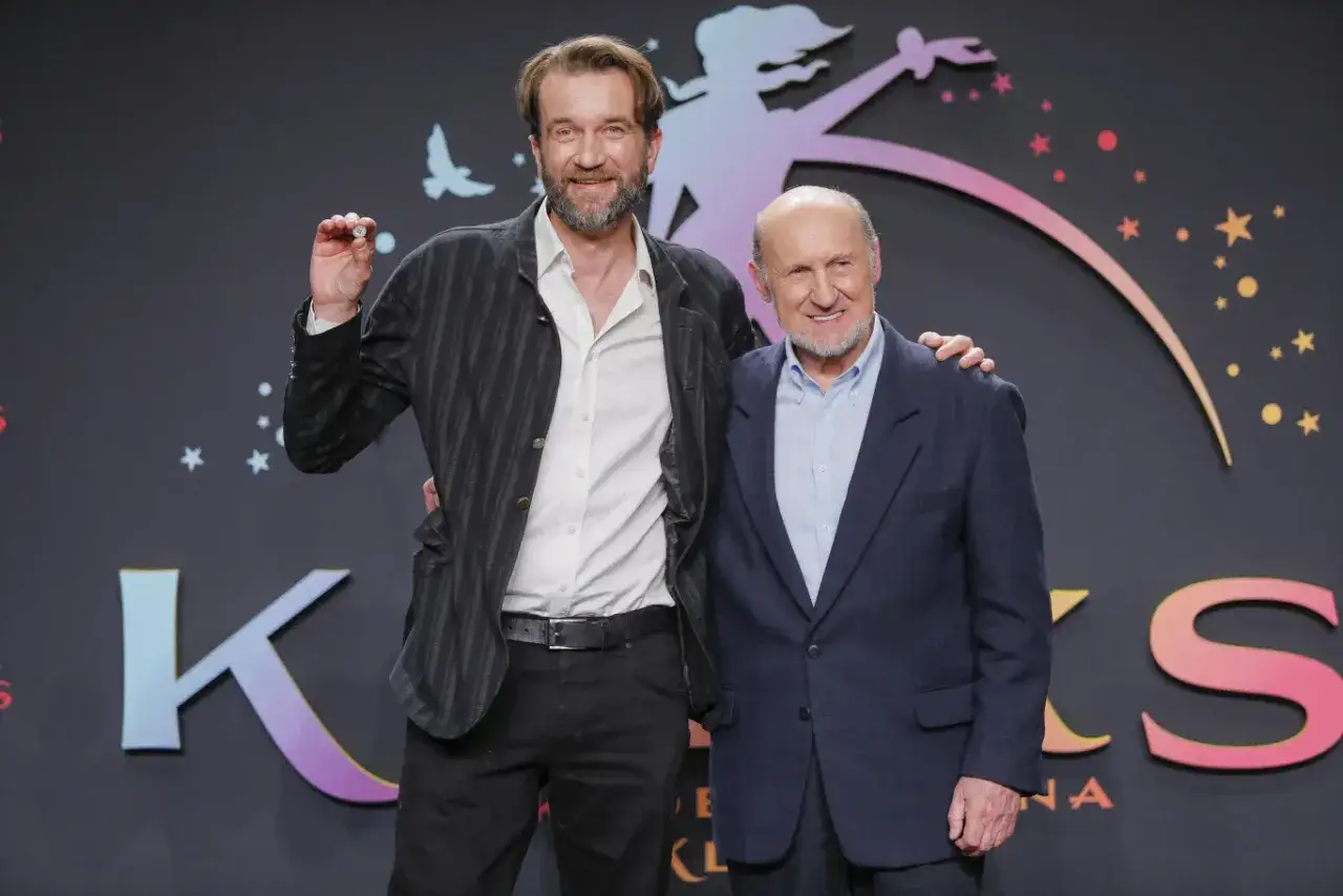Piotr Fronczewski i młodszy aktor pozują na tle scenografii z napisem 