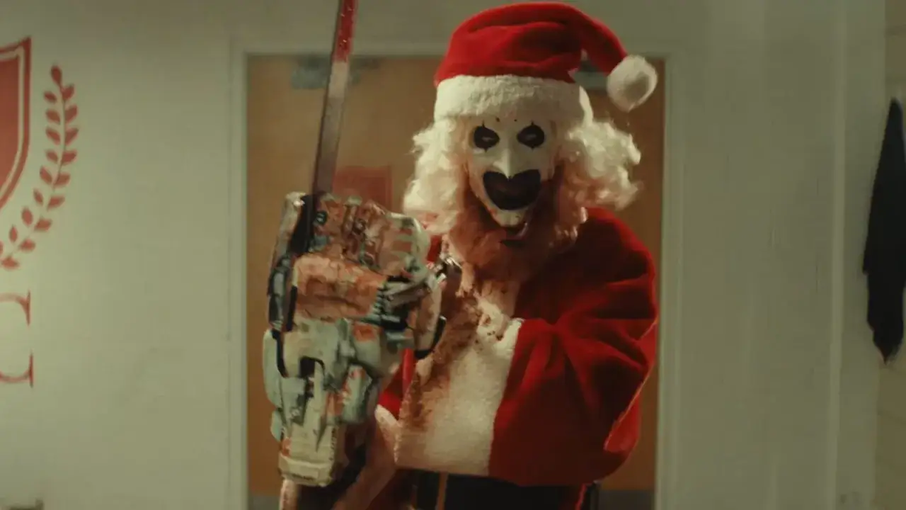 Artysta grozy Art the Clown w stroju Mikołaja, z zakrwawioną piłą mechaniczną, zapowiada nadchodzący horror Terrifier 3.
