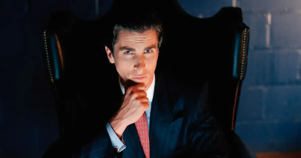 Patrick Bateman w garniturze, z ręką pod brodą, zastanawia się, czy patrick bateman naprawde zabijał.