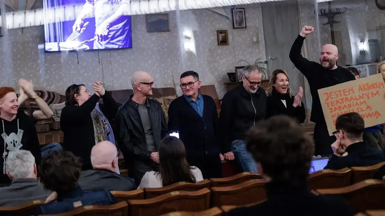 Aktorzy teatralni protestują, pytając, ile zarabiają. Na ekranie widać fragment spektaklu.