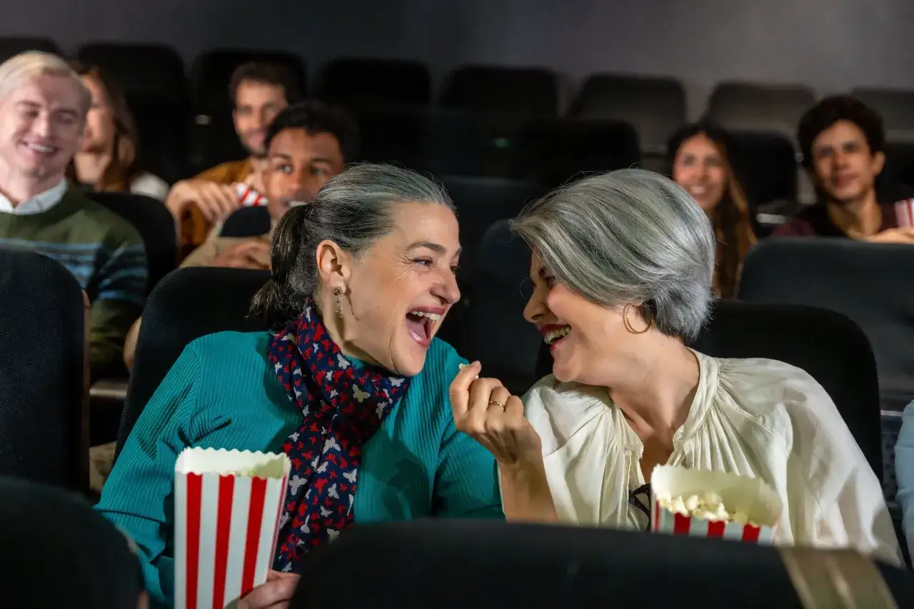 Dwie kobiety śmieją się, jedząc popcorn w kinie, czekając na premiery kinowe 2026.